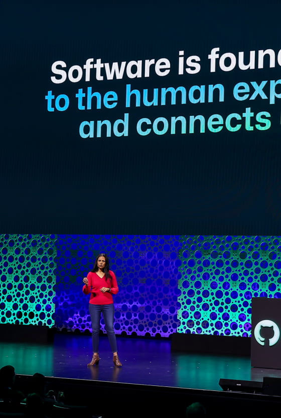 A woman presenting at a tech conference with a backdrop reading 'Software is foundational to the human experience and connects us.