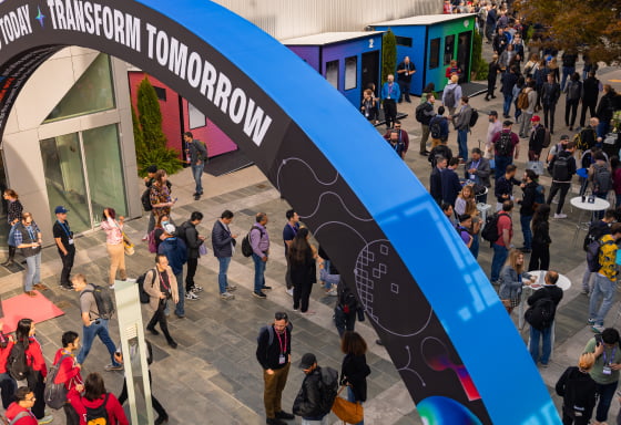 People mingling outside at a tech event near an arch with the words 'Today | Transform Tomorrow' and abstract digital designs.